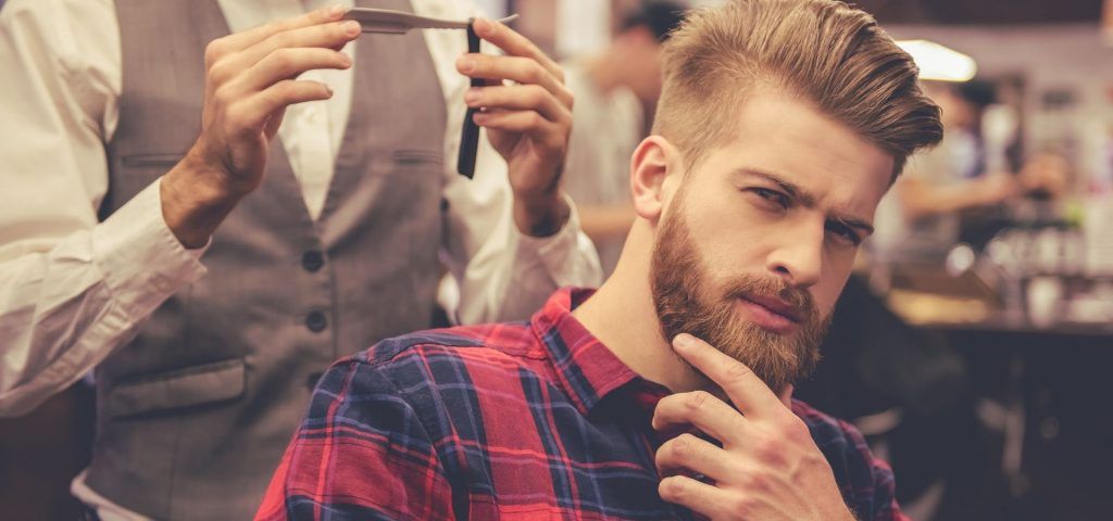 A man with a beard relaxes in a barber shop in Fort Lauderdale and Coral Gables enjoying a haircut.
